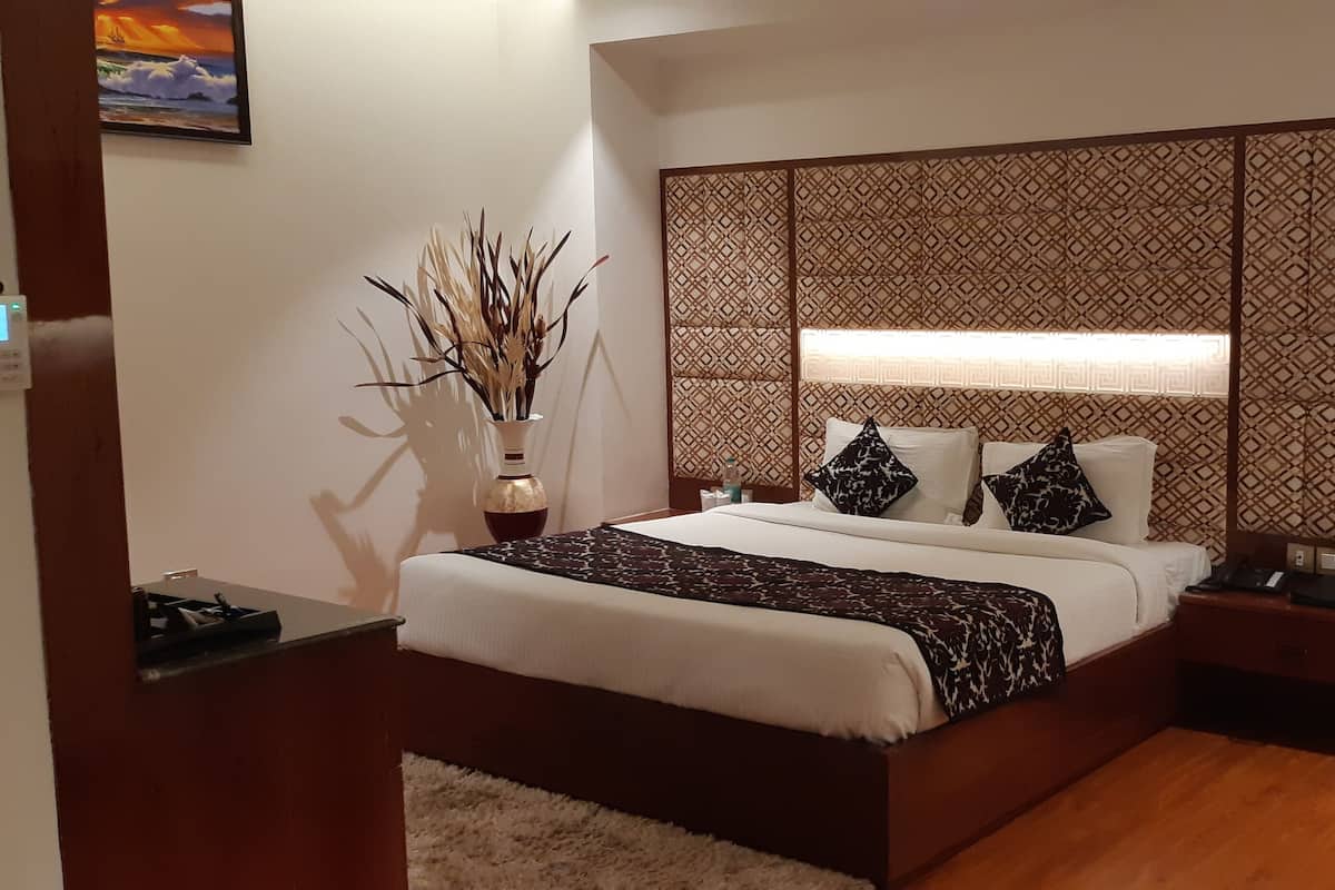 A neatly arranged bedroom with a bed, bedside tables, a decorative wall panel, and a vase with dried plants.