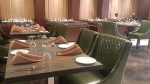 Uma sala de jantar com cadeiras estofadas em verde, mesas bem arrumadas com copos de vinho, pratos e talheres.