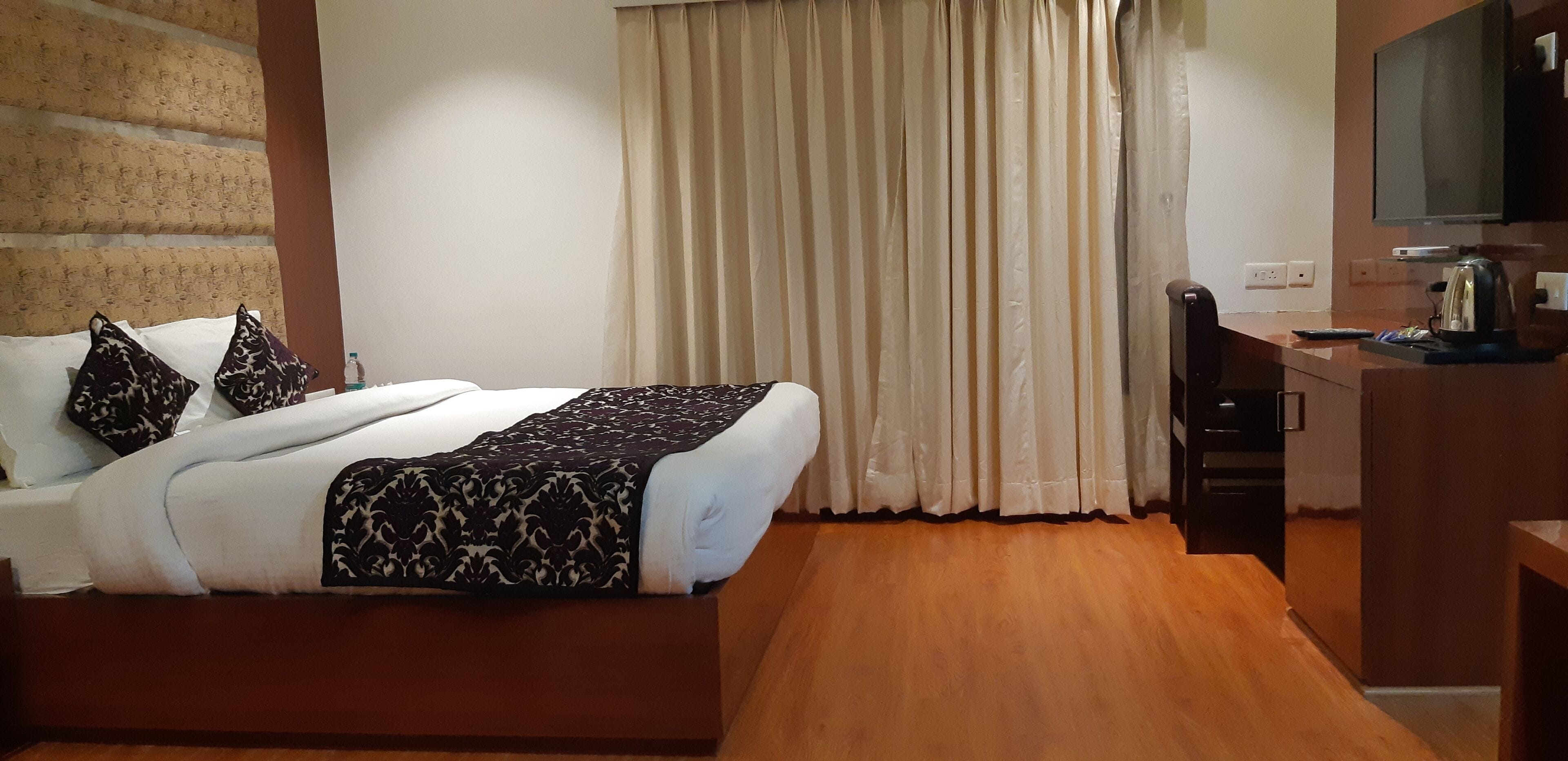 A hotel room with a bed, a desk, a television, and a window with curtains.