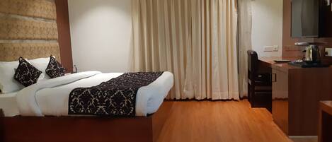 A hotel room with a bed, a desk, a television, and a window with curtains.