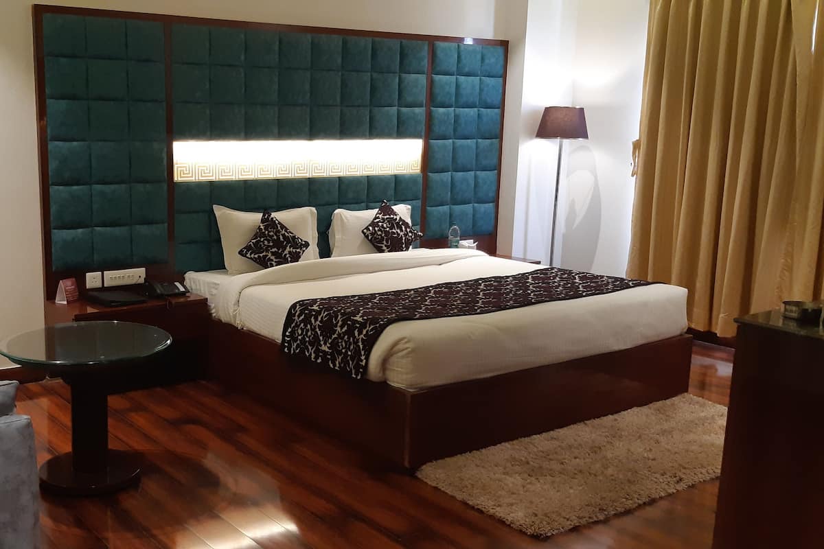 A hotel room with a large bed, a small round table, a sofa, and a decorative vase with dried plants.