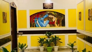 A hallway with a mural, potted plants, and a sign indicating a conference hall, restaurant, and banquet hall. - Prayag Inn (Prayagraj)