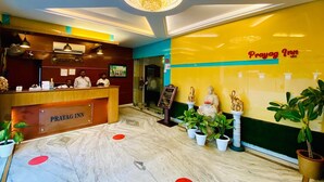 A reception area with a marble floor, a reception desk labeled "Prayag Inn," a chandelier, and a Buddha statue. - Prayag Inn (Prayagraj)