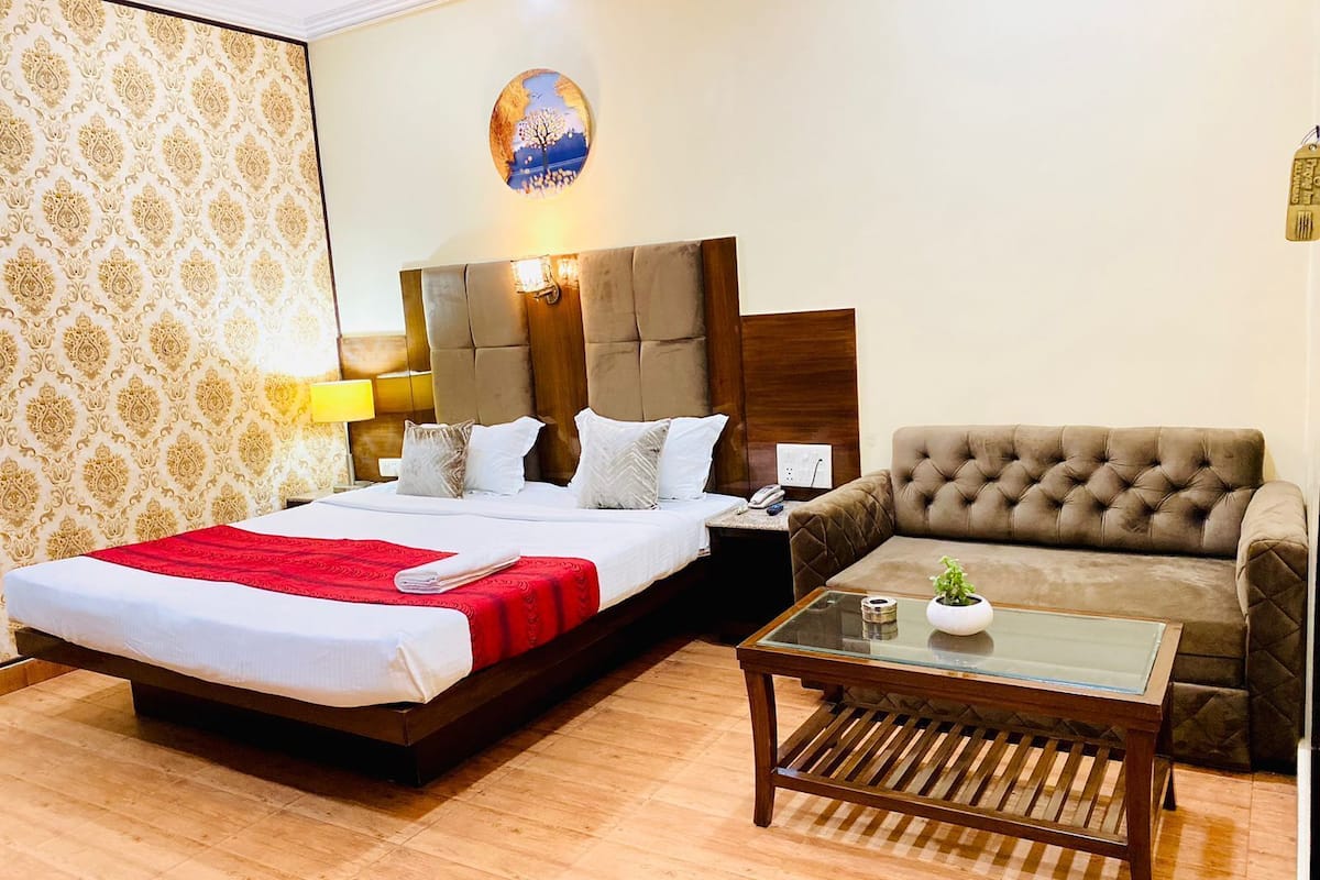 A hotel room with a large bed, a sofa, a small table, and a wall with a decorative panel.