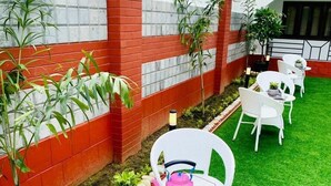 A patio with a white chair, a pink kettle, and a table set with drinks and a book titled "Spiritual". - Prayag Inn (Prayagraj)