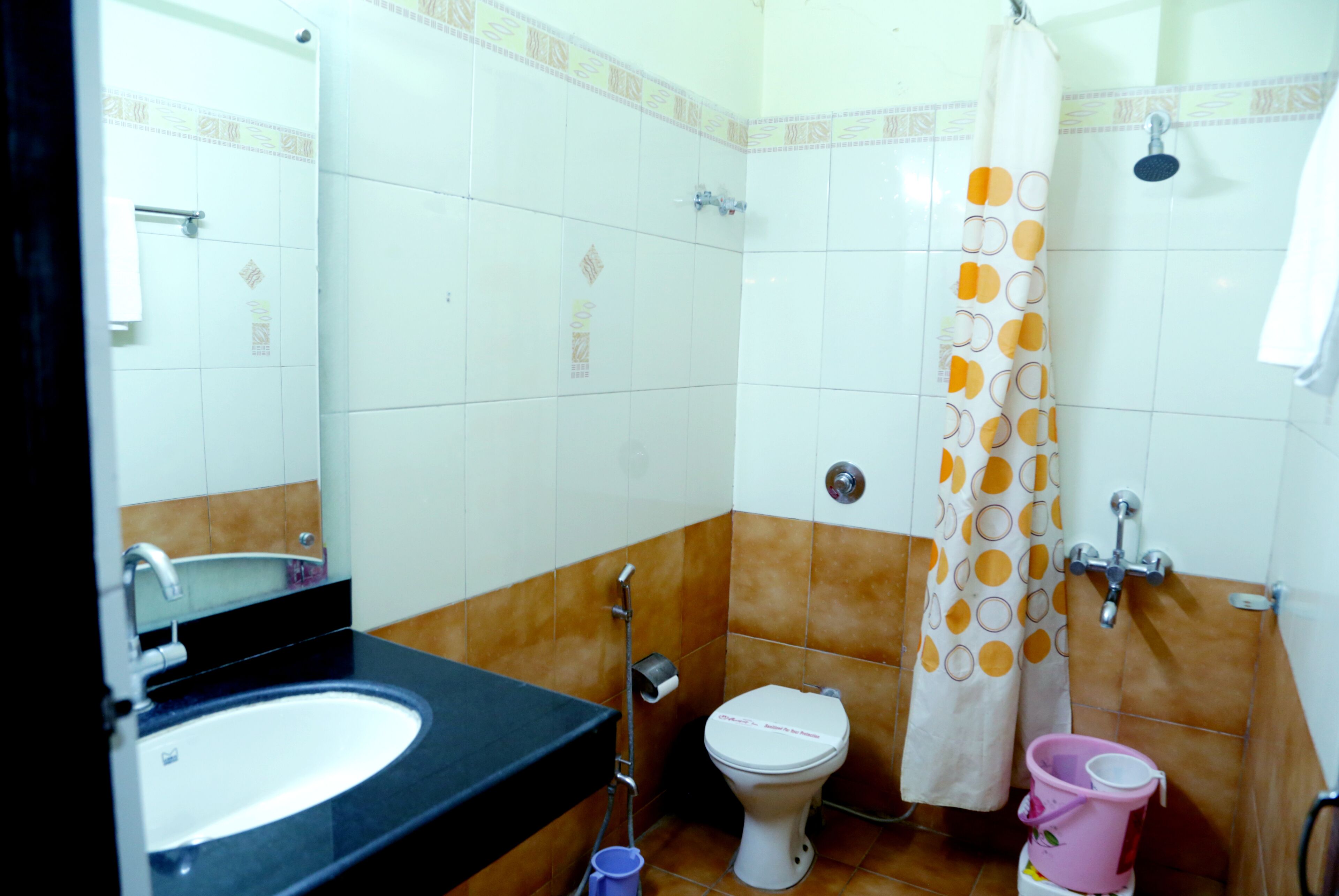 A bathroom with a sink, toilet, shower, and a pink bucket.