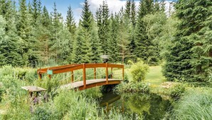 A wooden bridge over a pond surrounded by dense forest. - Retreat with Sauna, Hot Tub (Jägersgrün)