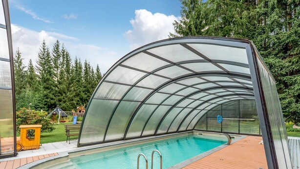 A covered swimming pool with a wooden deck, surrounded by trees. - Retreat with Sauna, Hot Tub (Jägersgrün)