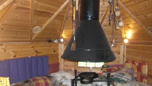 A cozy cabin interior with a wood stove, a purple cushioned bench, and a sleeping area with a colorful blanket. - Retreat with Sauna, Hot Tub (Jägersgrün)