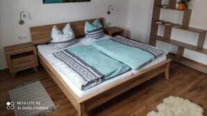 A neatly arranged bedroom with a wooden bed, matching nightstands, a wall-mounted lamp, and a framed landscape painting. - Vacation apartment Hartmann (Gohrisch)
