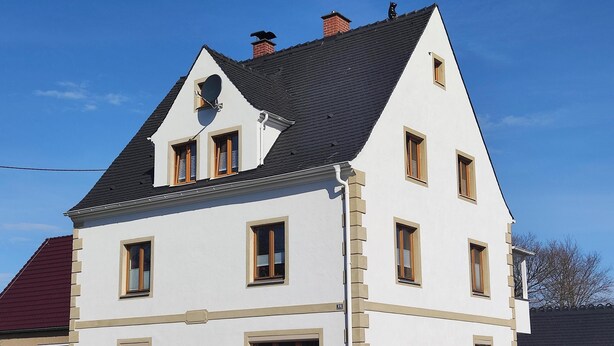 A two-story house with a steeply pitched roof, multiple windows, and a visible chimney. - Vacation apartment Hartmann (Gohrisch)