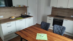 A modern kitchen with white cabinets, a wooden countertop, a dining table with chairs, and a TV mounted above the counter. - Vacation apartment Hartmann (Gohrisch)