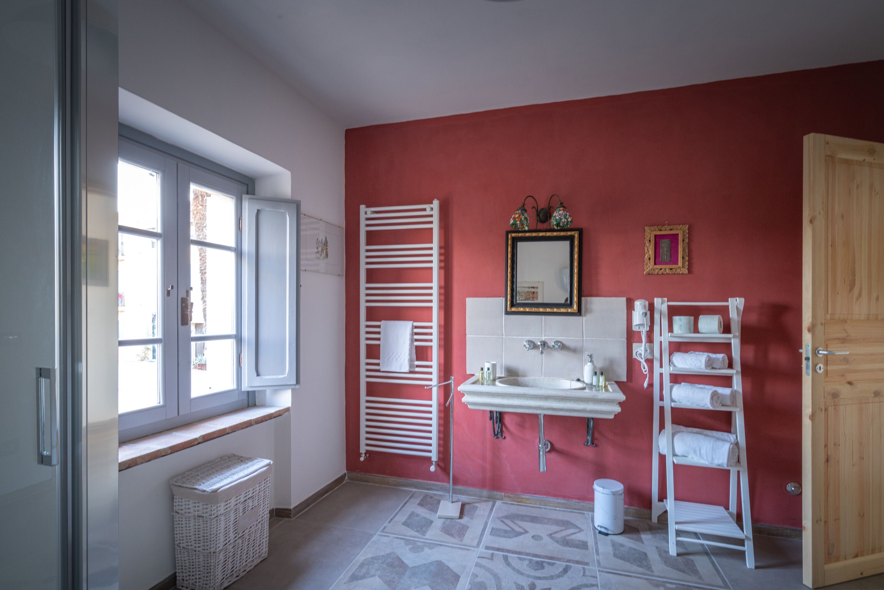 Une salle de bain avec un mur rouge, un lavabo blanc, un miroir et une porte en bois.
