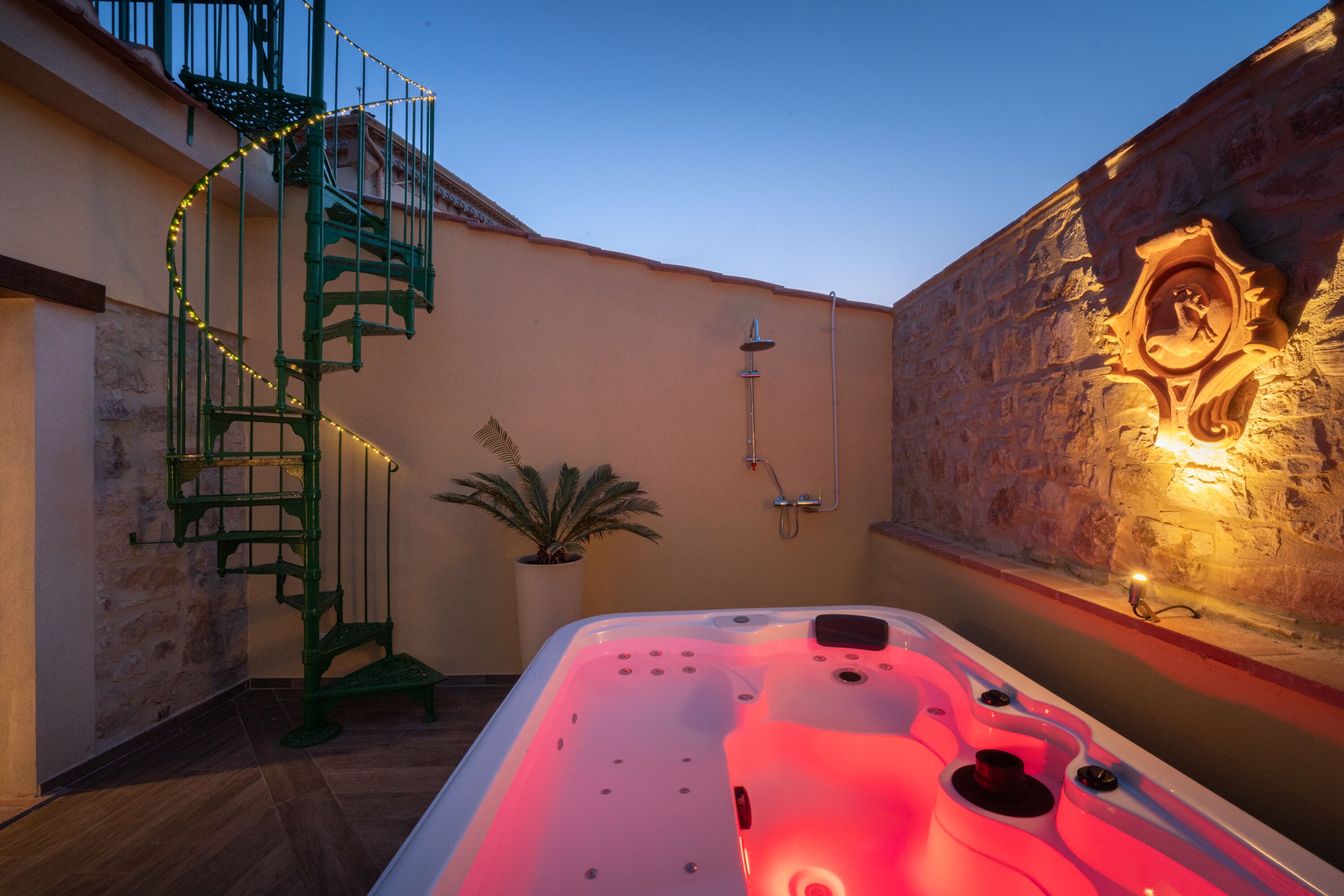 Uma área de spa com hidromassagem, escadaria em espiral e parede de pedra com um emblema esculpido.