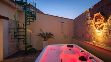 Uma área de spa com hidromassagem, escadaria em espiral e parede de pedra com um emblema esculpido.