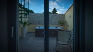 En terrasse med et spabad, to krukker med planter og en foldestol.