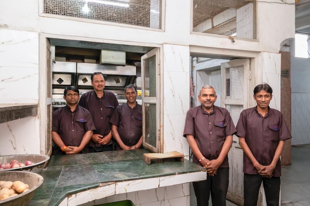 A group of men standing in a kitchen area with marble countertops and a large window.