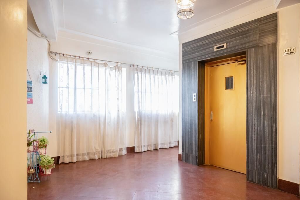 Eine Hotelhalle mit Holzboden, einem gelben Aufzug und einem Fenster mit transparenten Vorhängen.