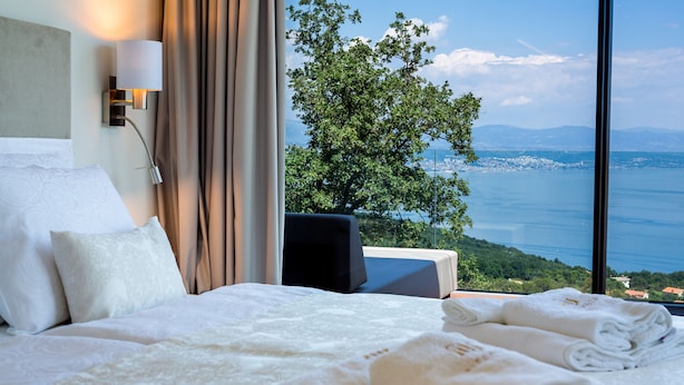 A hotel room with a bed, a nightstand, a lamp, and a view of a tree and water. - Villa AltaVista - Seaview & Relax with Private MiniGolf & Wellness (Poljane)