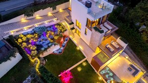 A modern two-story house with a rooftop deck, a landscaped garden with colorful lights, and a well-lit exterior. - Villa AltaVista - Seaview & Relax with Private MiniGolf & Wellness (Poljane)