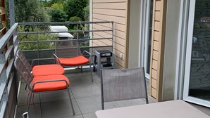 A balcony with two chairs and a table, overlooking a garden and a building. - Central Apartment in Biscarrosse - 4 Guests, Close to Beaches, Surf Classes, Parking & Wifi Included (Biscarrosse)