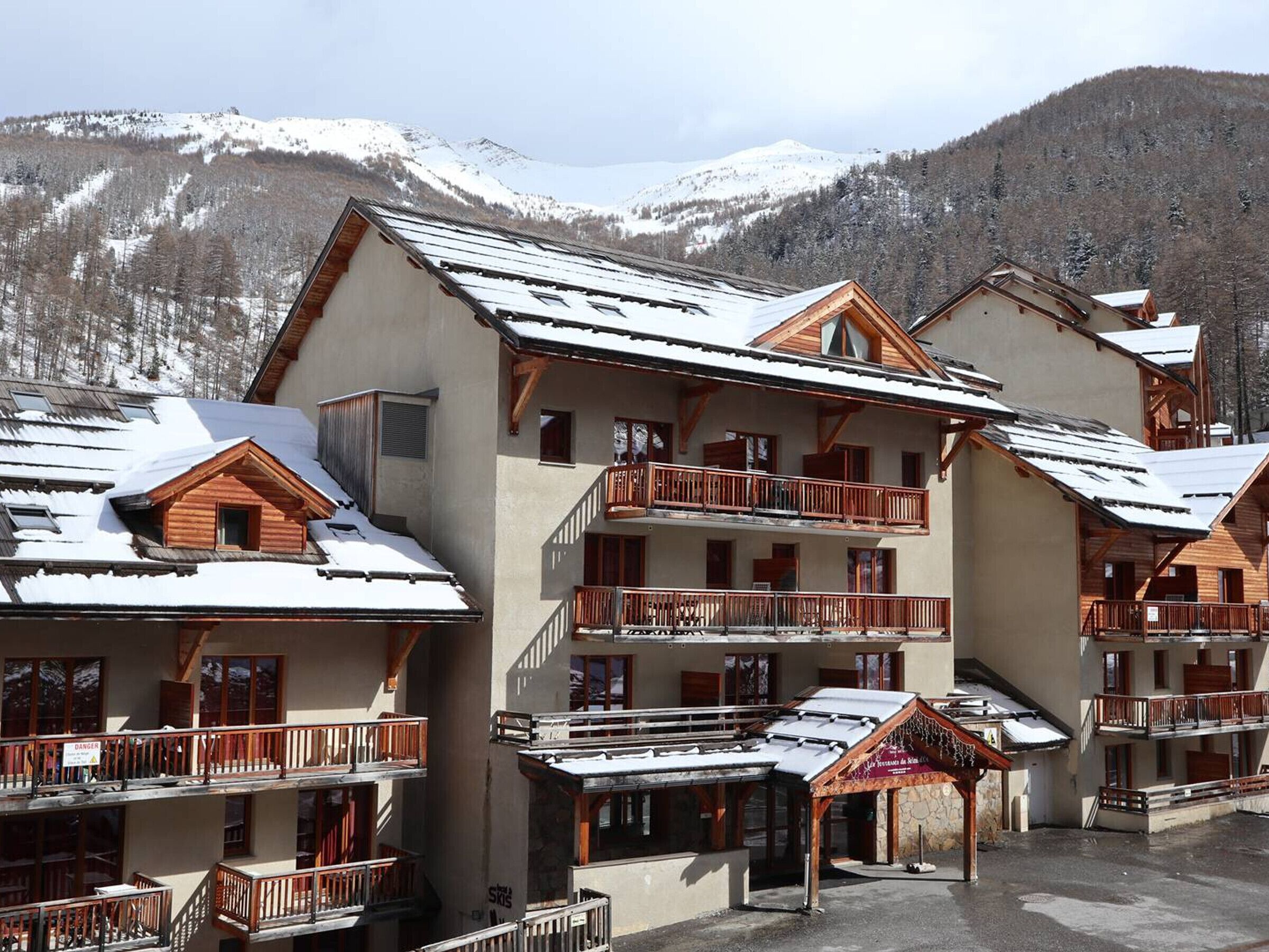 A multi-story hotel with wooden balconies and a ski resort backdrop.
