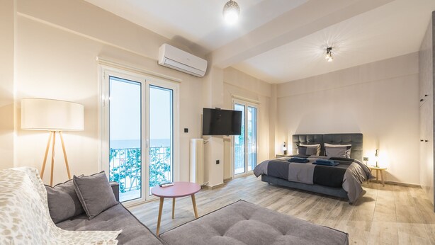 Et moderne hotelværelse med sofa, et lille bord, en seng med gavl, et fjernsyn og en balkon med udsigt.