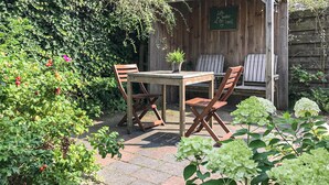 A wooden table and four chairs in a garden setting with a wooden fence and greenery. - Beach front home in Bergen aan Zee (Bergen aan Zee)