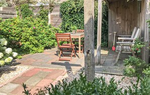 Eine Terrasse mit Holzküchenstühlen und einem Tisch, umgeben von einem Garten mit verschiedenen Pflanzen und einem Holzzaun.