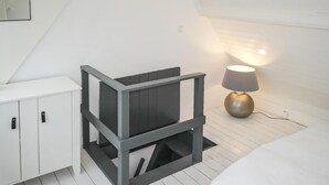 A small, white room with a sloped ceiling, a white cabinet, a grey and black storage unit, and a table lamp. - Beach front home in Bergen aan Zee (Bergen aan Zee)