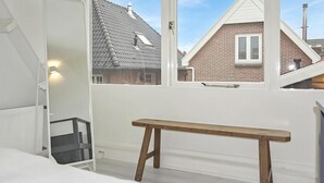 A bedroom with a wooden bench, a window with a view of neighboring houses, and a white radiator. - Beach front home in Bergen aan Zee (Bergen aan Zee)