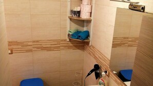 Une salle de bain équipée de toilettes, d’un lavabo et d’étagères où sont rangées les serviettes et les articles de toilette.