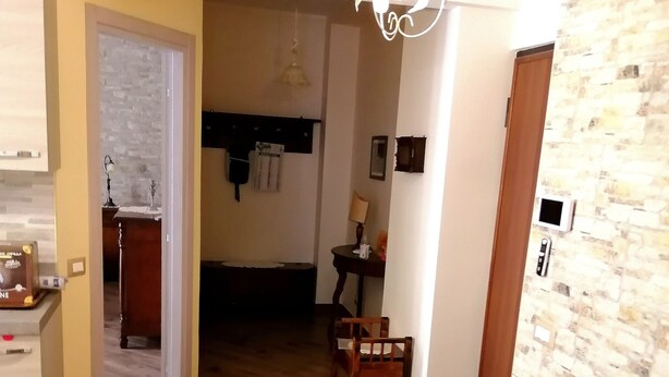 Un salon doté d’un plancher en bois, d’un canapé agrémenté de coussins à motifs floraux, d’un luminaire suspendu et d’un mur imitant la pierre.