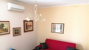 Un salon avec un canapé rouge, un plancher en bois et un climatiseur fixé au mur.