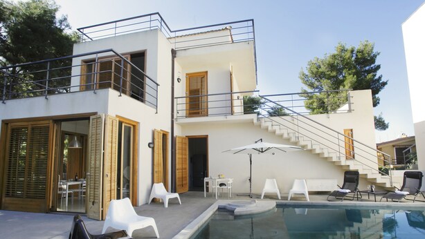 Une maison moderne à deux étages, dotée d’une piscine, d’un espace de détente extérieur et d’un escalier menant à un balcon.