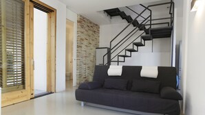 Un salon moderne avec un canapé foncé, une porte en bois, un mur en briques et un escalier doté de rampes noires.