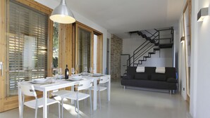 Un espace repas moderne avec une table blanche dressée pour quatre personnes, un escalier et un canapé de couleur sombre.