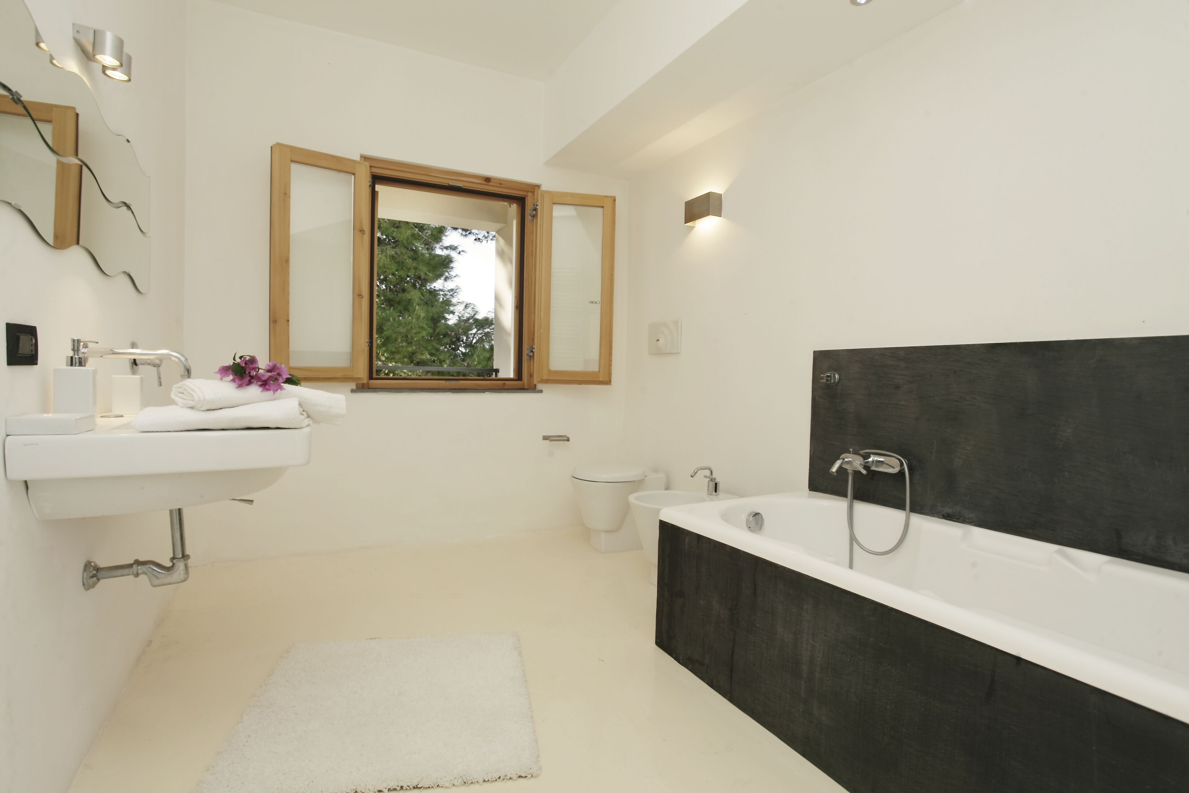 Une salle de bain moderne avec un lavabo blanc, une grande baignoire et une fenêtre avec des cadres en bois.