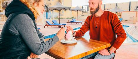 Una pareja cenando en una mesa al aire libre, con una piscina al fondo.