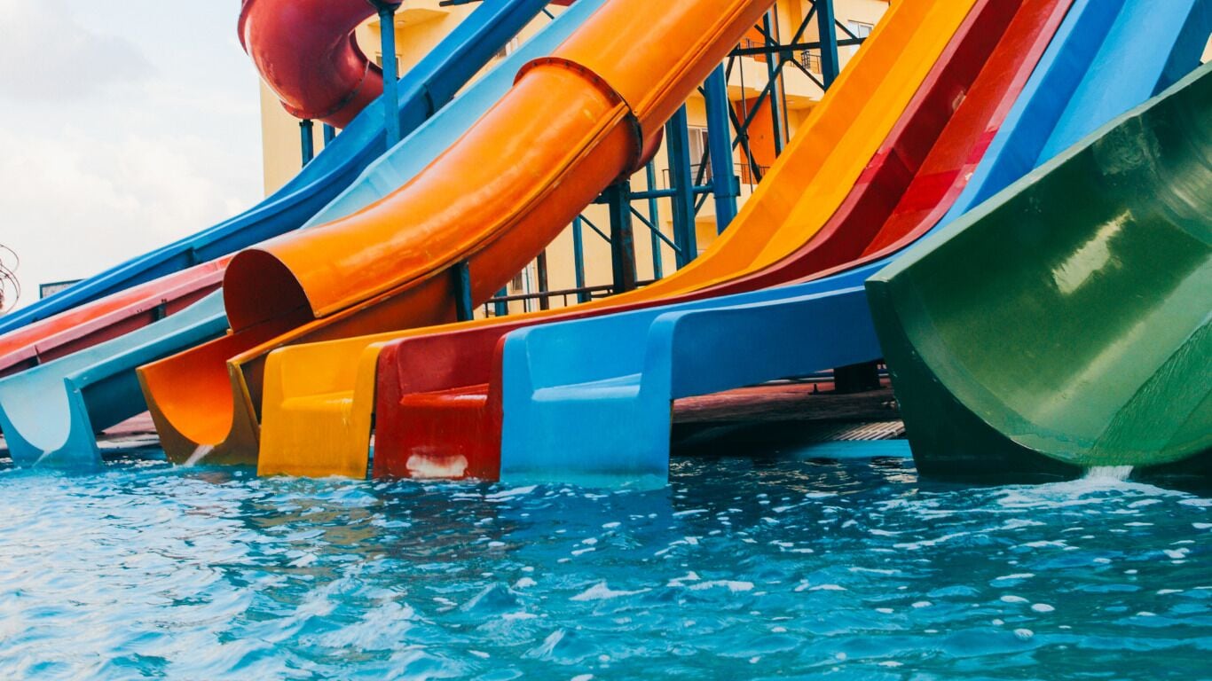 Un tobogán acuático con múltiples carriles de varios colores, incluyendo naranja, azul y verde, sobre una piscina.