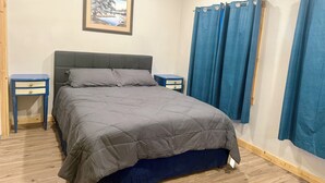 Un dormitorio con una cama, dos mesitas de noche, un cuadro en la pared y cortinas azules.