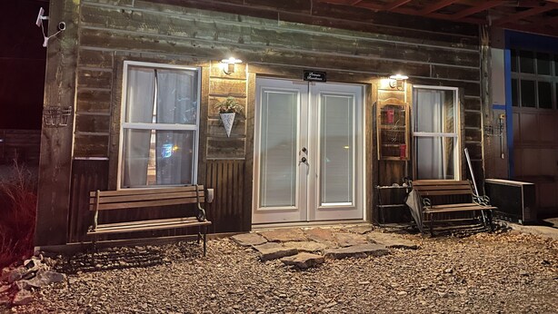 Una cabaña rústica con dos grandes puertas de vidrio, una banca afuera y una pequeña zona de porche.