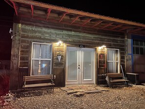 Eine rustikale Holzhütte mit zwei großen Glasüren, einer Bank davor und einer kleinen Veranda.