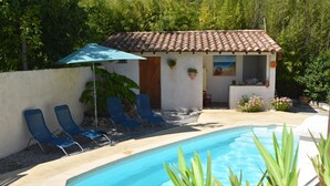 A swimming pool with blue water, surrounded by blue lounge chairs and a small building with a tiled roof.