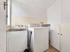 A compact kitchen with a sink, a washing machine, and cabinets. - Pearl Beach Semi - 2 min to sand & sea – Lilly (Pearl Beach)