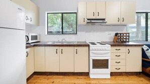 Cocina compacta con gabinetes blancos, microondas, estufa y ventana que proporciona luz natural.