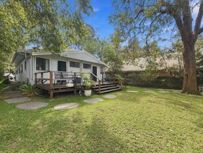 A single-story house with a deck, outdoor seating, and a large tree in the yard.