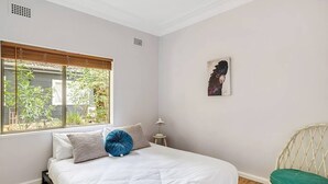 Un dormitorio con una cama, una ventana con persianas, una mesita auxiliar y una silla.