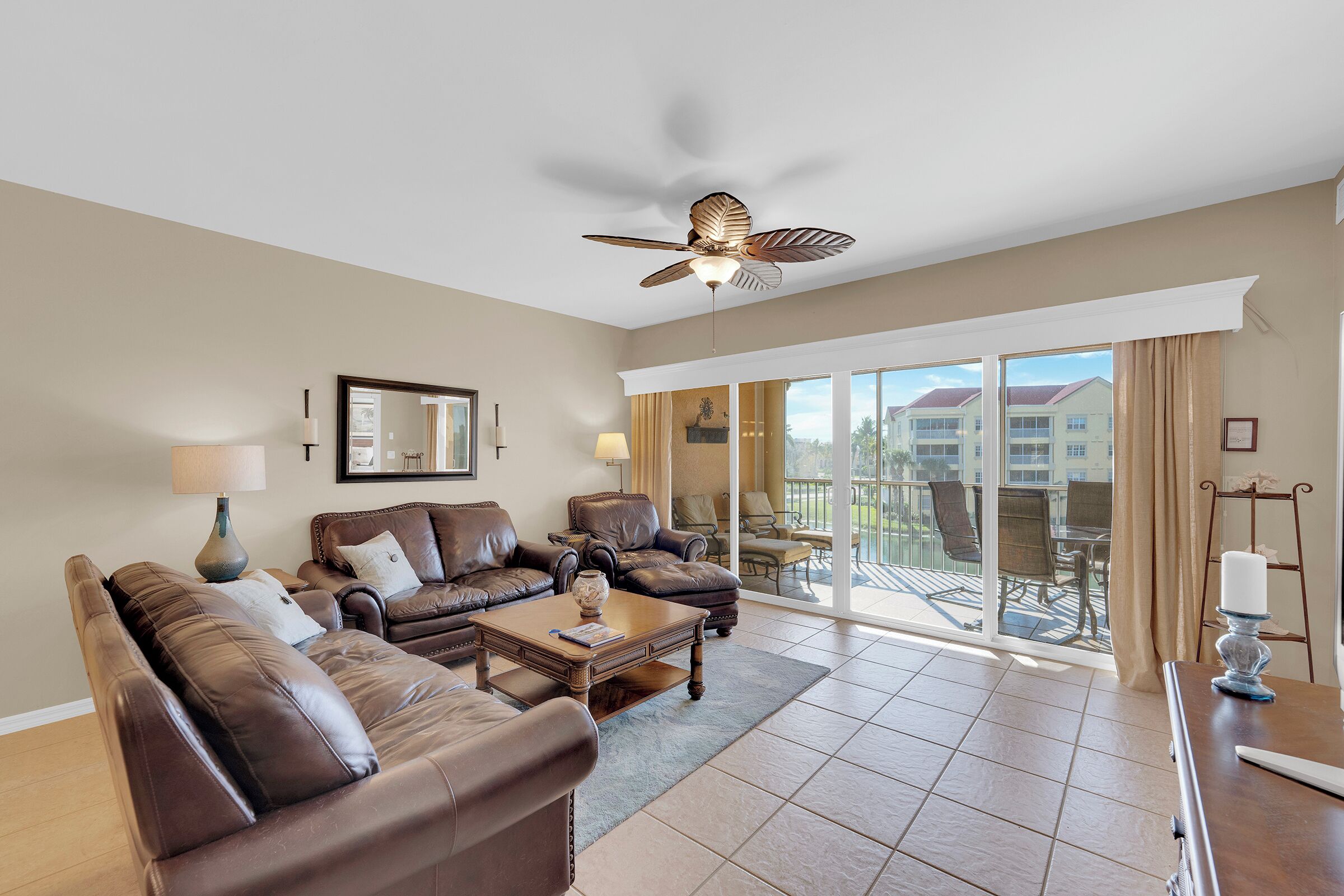 A spacious living room with leather sofas, a coffee table, and a ceiling fan.