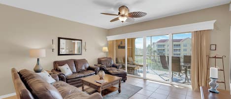 A spacious living room with leather sofas, a coffee table, and a ceiling fan.